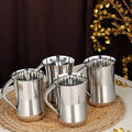 Set of four stainless steel kitchen utensils mugs on a woven mat, table setting
