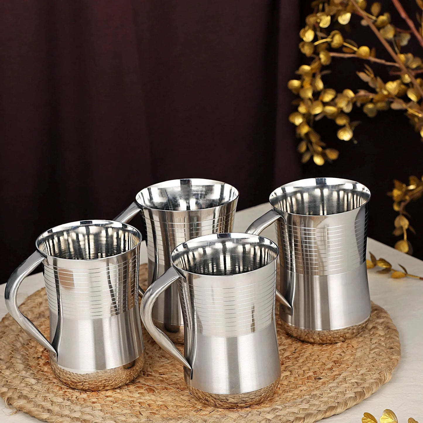 Set of four stainless steel kitchen utensils mugs on a woven mat, table setting