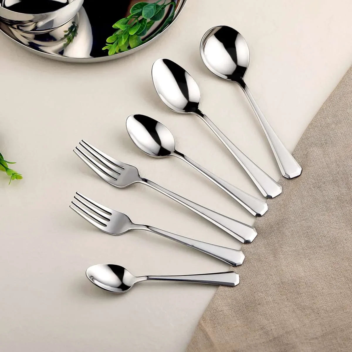 Stainless steel kitchen utensils set with spoons and forks on a beige background